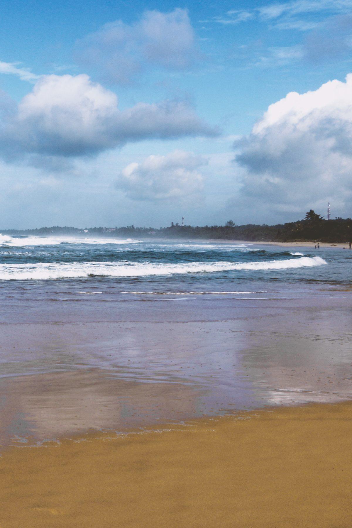 Waves rolling onto an empty beach under a blue sky