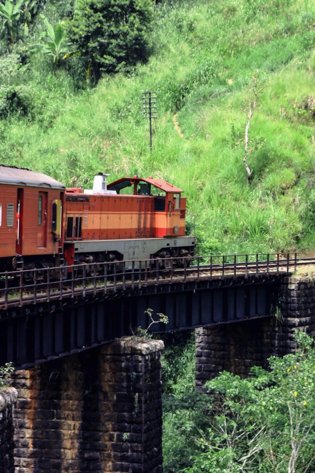 A red train engine crossing a black iron bridge