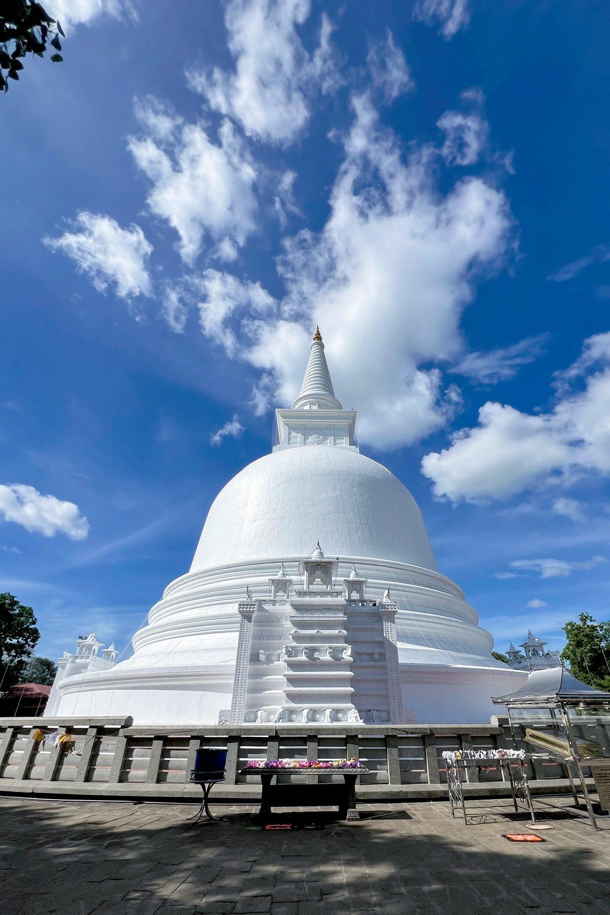 Mahiyangana stupa, white against a deep blue sky full of clouds