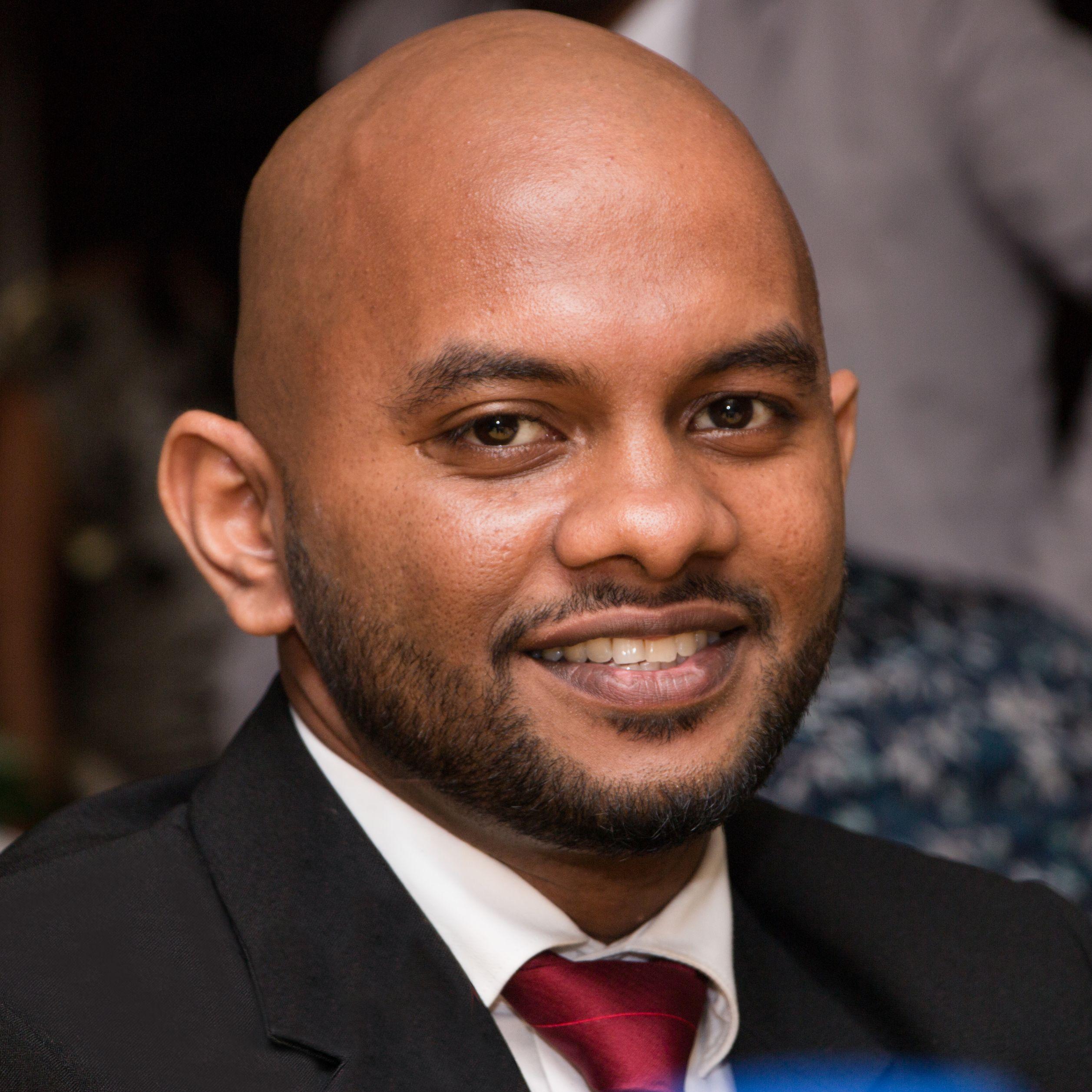 Portrait of Hashan smiling, in a dark suit